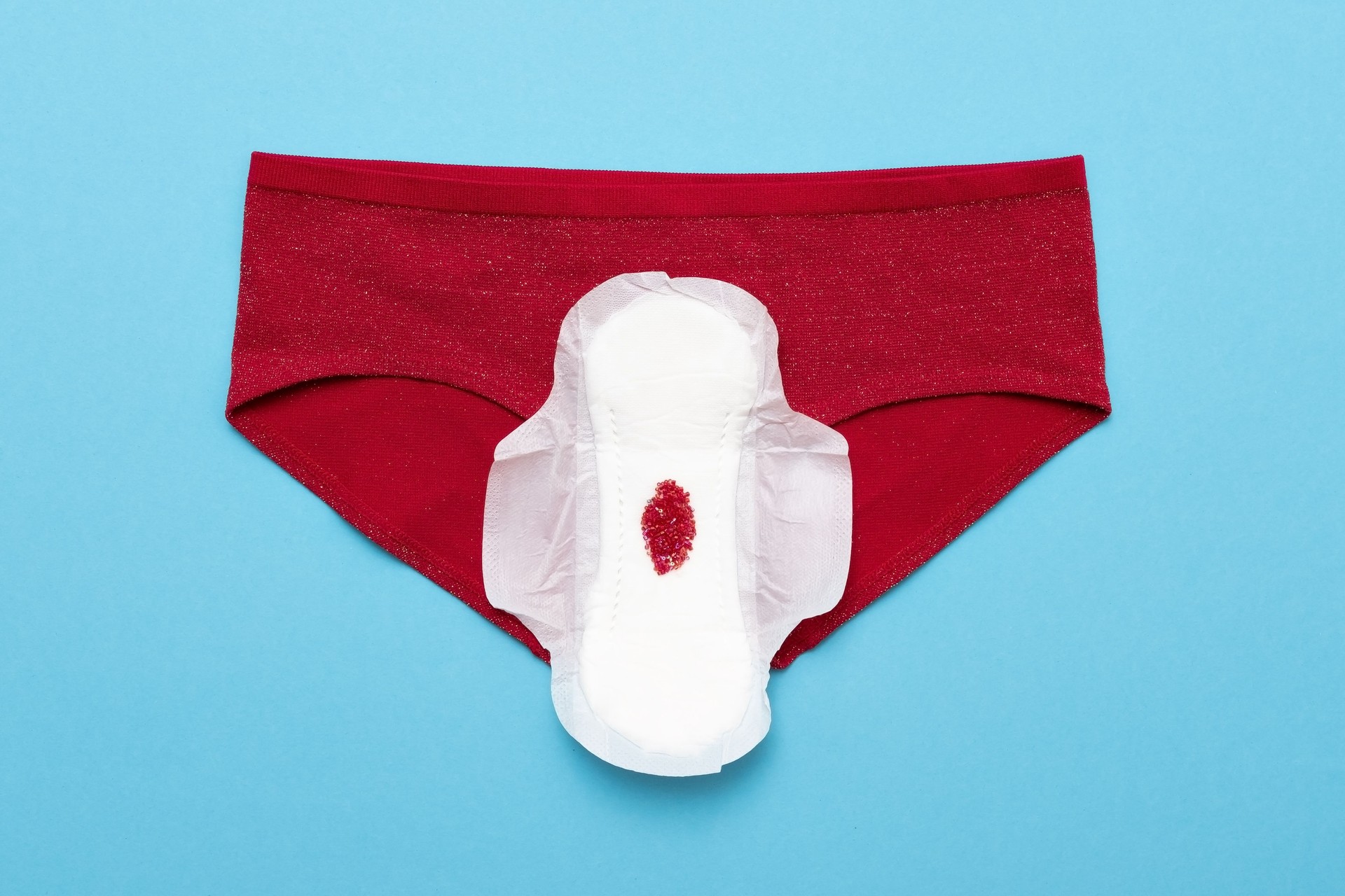 Red drop from beads on pants on blue background. Menstruation period